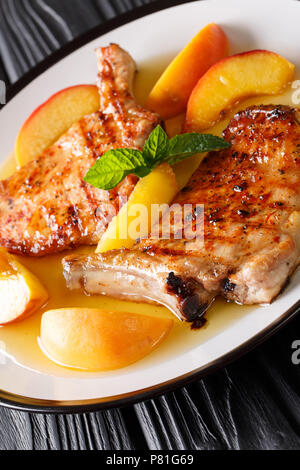 Schweinefleisch vom Grill mit glasierten Pfirsichen und Honig Knoblauch Sauce schließen chop - bis auf einen Teller auf dem Tisch. Vertikale Stockfoto