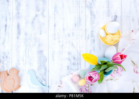 Köstliche Frühling Frühstück auf einem weißen Hintergrund. Strauß mit frischen Tulpen. Kleine und Große bunte Ostereier. Haferflocken, Kaffee, frischen Beeren. Postkarte für Ostern. Stockfoto