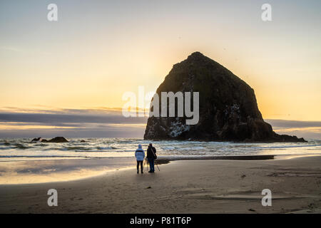 Fotograf mit Stativ warten auf Sonnenuntergang am Haystack Rock, iconic Meer Stack der Pazifischen Nordwesten, Cannon Beach, Oregon, USA. Stockfoto