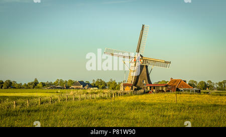 Holländische Windmühle aus Holz mit kleinen Miller Haus bei Sonnenuntergang im Sommer mit Blumen. Vintage Farbe Stockfoto