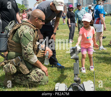 JERSEY CITY, N.J. (29. Mai 2016) - die Beseitigung von Explosivstoffen Techniker 3. Klasse Abraham Ruiz, für die Beseitigung von Explosivstoffen Mobile Einheit 12 zugeordnet, hilft einem Kind erhalten einen Ball Cap aus einem PackBot transportable Robotik System während einer Luftfahrt Demonstration an Liberty State Park, N.J. im Rahmen der Fleet Week New York 2016. Flotte Woche, jetzt im 28. Jahr, ist die Stadt der Zeit - Feier des Meeres Leistungen geehrt. Es ist eine einmalige Chance für die Bürger von New York und die umliegenden Tri-state-area Seemänner, Marinesoldaten und Küstenwache sowie Zeugen aus erster Hand zu erfüllen Stockfoto