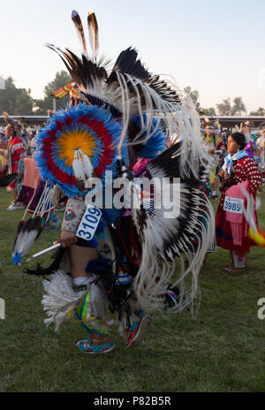 Ein eingeborener amerikanischer Mann Pow Wow dancer von hinten mit einer Frau in einem Elch Zahn Kleid im Hintergrund fotografiert. Stockfoto