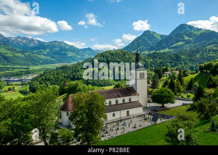 Blick von der Burg von Gruyeres auf eine Kirche und Friedhof unterhalb von wunderschönen Alpen umgeben. Stockfoto