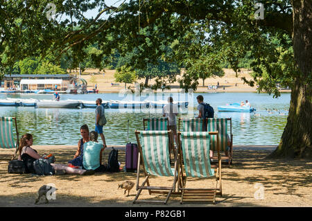 Sonnenanbeter und Wanderer im Hyde Park, London, UK, mit der Serpentine im Hintergrund, während der Juli 2018 Hitzewelle Stockfoto