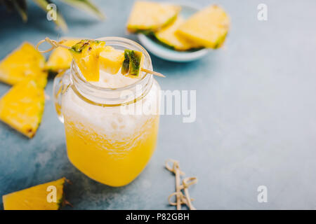 Saftige Sweet Summer Drink Cocktail mit Ananas und Eis im Glas auf blauen Tabelle. Stockfoto