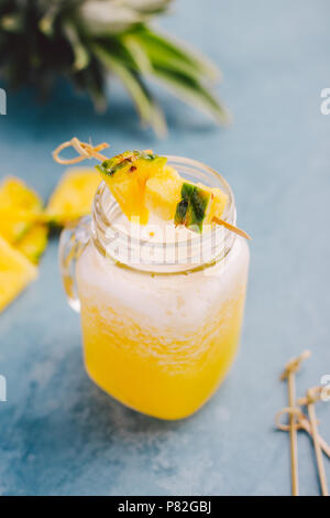 Saftige Sweet Summer Drink Cocktail mit Ananas und Eis im Glas auf blauen Tabelle. Stockfoto