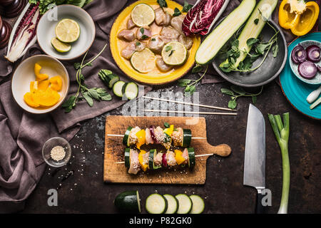 Vorbereitung der verschiedenen hausgemachten Huhn Fleisch Gemüse Spieße für Grill oder bbq auf rustikalen Hintergrund mit Zutaten, Teller, Schneidebrett und Kit Stockfoto