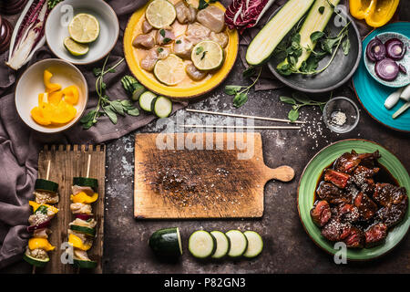 Vorbereitung der verschiedenen hausgemachten Fleisch Gemüse Spieße für Grill oder bbq auf rustikalen Hintergrund mit Zutaten, Teller, Schneidebrett und Küche zu Stockfoto