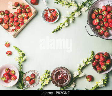 Rahmen mit frischen Erdbeeren im Sieb und Schüsseln mit Jam jar und Löffel auf dem Küchentisch Hintergrund mit Garten Blumen, Ansicht von oben. Sommer berr Stockfoto