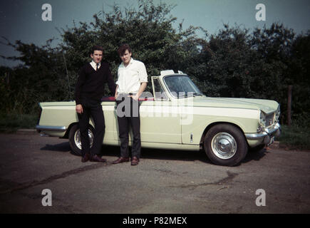 Ende der 1960er Jahre, zwei junge Männer stehen durch ein britisches Auto gebildet, ein Triumph Herald 13/60 Cabrio motorcar, England, UK und die standard-triumph Co von Coventry. Diese Version, die drop-Kopf, war aber zu diesem Zeitpunkt war die 1300-cm³-Motor wurde im Vergleich zu anderen Unter-. Stockfoto