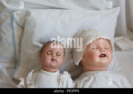 Zwei gruselige alte Puppen, die aussehen, als ob Sie schlafen in einem Bett. Stockfoto