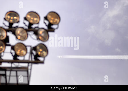 Flugzeug fliegen in den blauen Himmel zwischen den Wolken und Sonnenschein. Vor dem Hintergrund der Strahler des Stadions Stockfoto