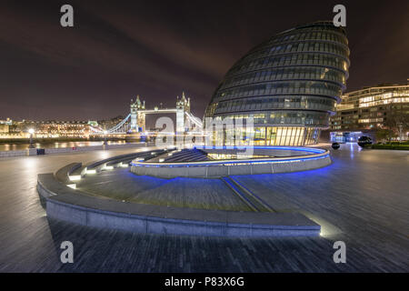 Treffpunkt an der Lufthutze Amphitheater an mehr London mit Rathaus und die Tower Bridge, die in blau und orange Leuchten an der Themse bei Nacht Stockfoto