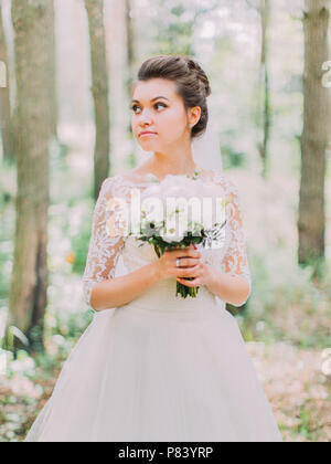 Brustbild der schwerwiegenden Braut mit der Wedding Bouquet ist neben der Suche im Wald. Stockfoto