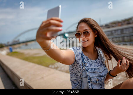 Ein schönes fröhliches Mädchen eine selfie und genießen auf der Stadt rivershore an einem schönen Sommertag. Stockfoto