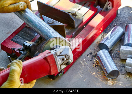 Ein Bauarbeiter mit einer Schleifmaschine auf einem neu geschnitten aus verzinktem Stahlrohr Stockfoto