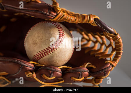 Nahaufnahme einer verwendet baseball ball innerhalb Braun, Leder baseball Handschuh auf schlichten, grauen Hintergrund. Stockfoto