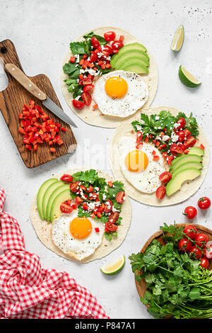 Tortilla mit Avocado, Salsa und Ei auf konkreten Hintergrund. Ansicht von oben Stockfoto