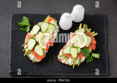 Spargel und Lachs Sandwiches auf einer Schiefertafel Hintergrund. Leckeres Sandwich mit geräuchertem Lachs, Frischkäse, Spargel und Gurken Stockfoto