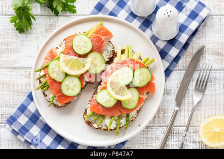 Lachs Toast mit Spargel, Käse und Gurke auf eine weiße Platte, Ansicht von oben. Leckeres Sandwich mit Lachs, Spargel und Käse Stockfoto