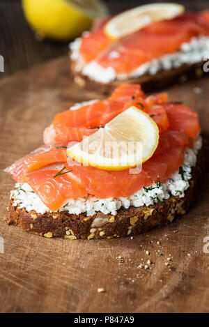 Lecker lachs Sandwich mit Frischkäse und Scheibe Zitrone auf Holzbrett, Detailansicht, selektiver Fokus Stockfoto