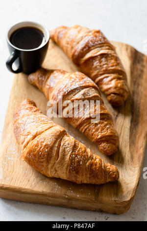 Croissants und Kaffee auf Holzbrett. Frisch gebackene Croissants. Französische Croissant und Tasse schwarzen Kaffee Espresso. Selektiver Fokus Stockfoto