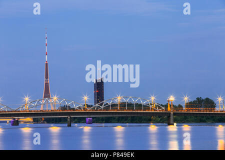 Riga, Lettland. Zwei Brücken über die Daugava zusammen: Stein Akmens und Eisenbahnbrücke In Abend-Beleuchtung mit roten Radio TV Tower Hintergrund im Sommer Stockfoto