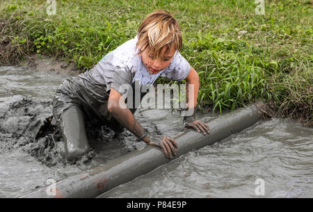 Biddinghuizen, Niederlande - 23. Juni 2018: Kind während einer mudrun (mudraise) im Schlamm und im Wasser klettern einen Baumstamm. Stockfoto