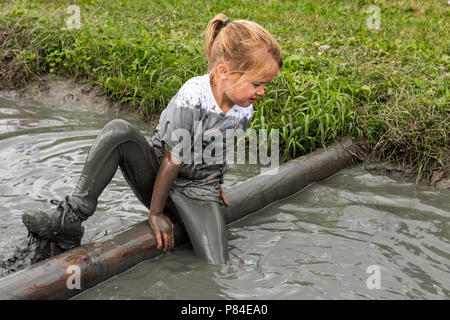 Biddinghuizen, Niederlande - 23. Juni 2018: Kind während einer mudrun (mudraise) im Schlamm und im Wasser klettern einen Baumstamm. Stockfoto