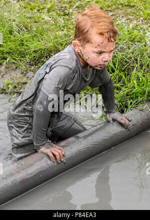 Biddinghuizen, Niederlande - 23. Juni 2018: Kind während einer mudrun (mudraise) im Schlamm und im Wasser klettern einen Baumstamm. Stockfoto