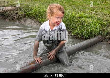 Biddinghuizen, Niederlande - 23. Juni 2018: Kind während einer mudrun (mudraise) im Schlamm und im Wasser klettern einen Baumstamm. Stockfoto