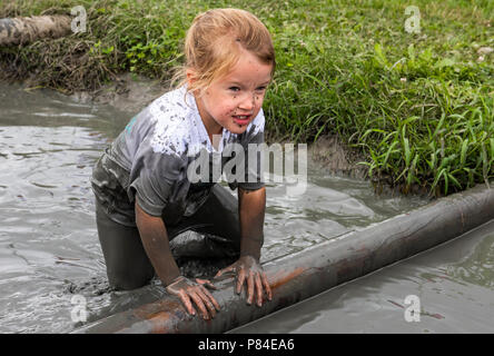 Biddinghuizen, Niederlande - 23. Juni 2018: Kind während einer mudrun (mudraise) im Schlamm und im Wasser klettern einen Baumstamm. Stockfoto