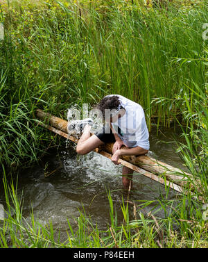 Biddinghuizen, Niederlande - 23. Juni 2018: Mann während eines Schlamm laufen (mudraise, Nächstenliebe) im Schlamm und im Wasser klettern einen Baumstamm. Stockfoto