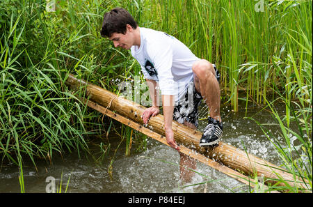 Biddinghuizen, Niederlande - 23. Juni 2018: Mann während eines Schlamm laufen (mudraise, Nächstenliebe) im Schlamm und im Wasser klettern einen Baumstamm. Stockfoto