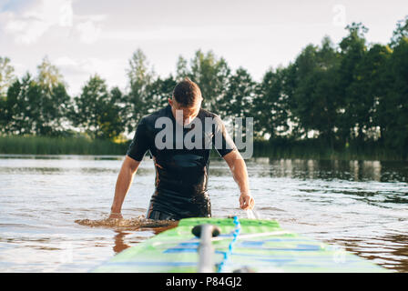 Ein Mann in einem Neoprenanzug entsteht aus dem Wasser, Paddle Boarding, SUP Board closeup Stockfoto