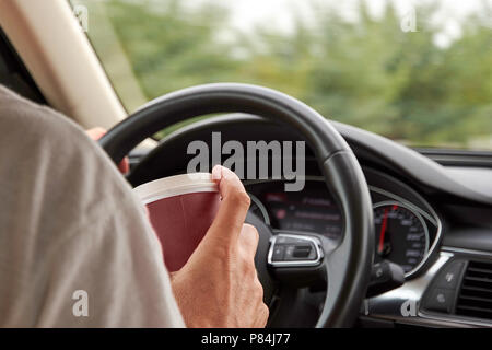 Der PKW-Fahrer hält eine Tasse in der Hand, mit dem Hintergrund einer unscharfen Rad Stockfoto