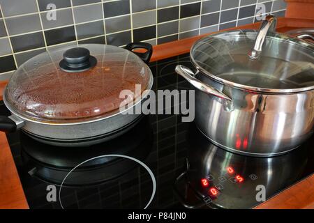 Schwarze Küche Induktionsherd mit Edelstahl Topf und Pfanne. Kochen in Töpfen auf Küche Herd mit modernen Fliesen. Stockfoto