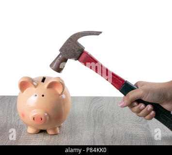 Eine Frau hält eine rostige Hammer ein Sparschwein auf dem hölzernen Tisch mit grauem Hintergrund zu zerschlagen. Stockfoto