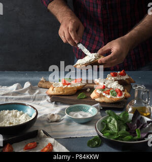 Man bereitet eine Italienische Bruschetta mit Tomaten, Basilikum und Käse auf dem Holzbrett Stockfoto