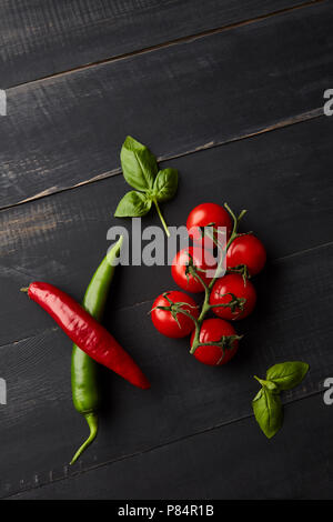 Eine Komposition aus frischem Gemüse, Tomaten, Chili und Basilikum auf einem dunklen Hintergrund. Flach Stockfoto