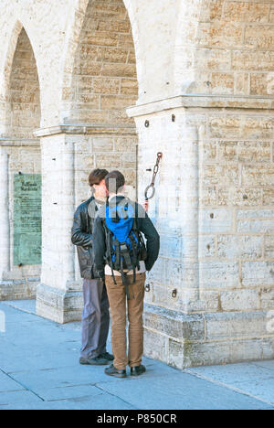 TALLINN, Estland - 1. Mai 2011: Zwei junge Männer schauen bei Metal Kragen und Ring für Hände und Füße auf den kleinen Pranger auf dem Rathaus an der Wand. Stockfoto