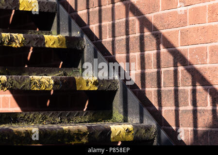 Nahaufnahme der Stufen mit schwarzen und gelben Warnstreifen. Verticalgestreifter Schatten, der durch Handlauf an die Wand geworfen wird Stockfoto