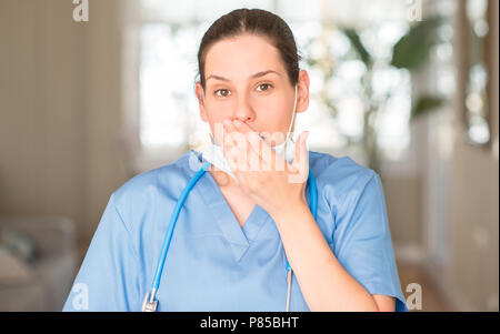 Junge Krankenschwester Frau mit maske und stethoskop Cover Mund mit der Hand mit Schande für den Fehler, den Ausdruck von Angst erschüttert, die in der Stille Angst, geheime con Stockfoto