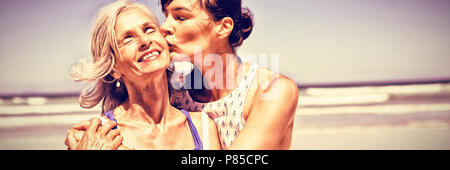 Junge Frau ihre Mutter am Strand küssen Stockfoto