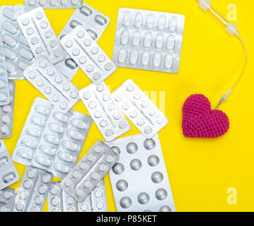 Rotes Herz und Katheter auf gelbem Hintergrund und Pakete mit weißen Tabletten, Nahaufnahme Stockfoto