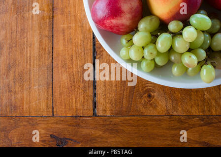 Schale mit Apfel-, Pfirsich- und Trauben von oben Blickwinkel auf Holz Textur Hintergrund gedreht. Gesunde Bio-Lebensmittel in hölzernen Tisch, mit Kopie Raum Stockfoto