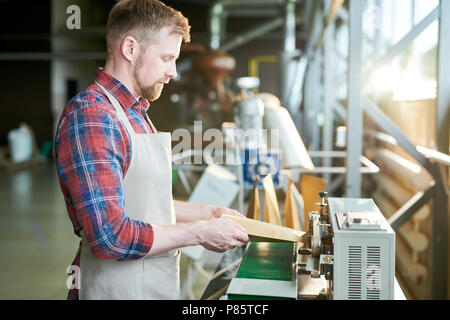 Seitenansicht Porträt des modernen bärtigen Mann mit Schürze Verpackung frisch gerösteten Kaffeebohnen in Handwerk Papiertüten beim Arbeiten in handwerklichen Rösterei Haus Stockfoto