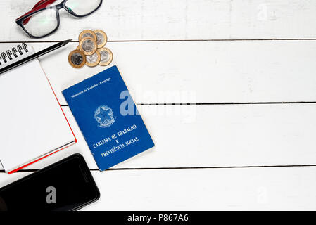 Arbeitserlaubnis, Notizblock, Bleistift, schwarz lcellphone, Gläser und einige Brasilianische einer echten Münzen auf weißem Hintergrund pinus Stockfoto