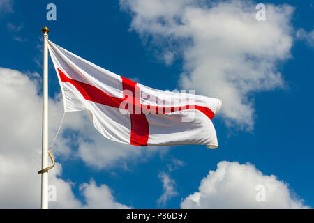 Das St George Flagge von England weht im breeye auf einem weißen flagpost vor einem blauen Himmel mit weißen Wolken Stockfoto