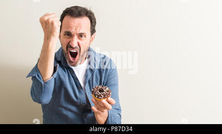 Älteren Menschen essen Schokolade Donut genervt und frustriert schrie mit Zorn, verrückt und schreien mit erhobener Hand, Wut Konzept Stockfoto